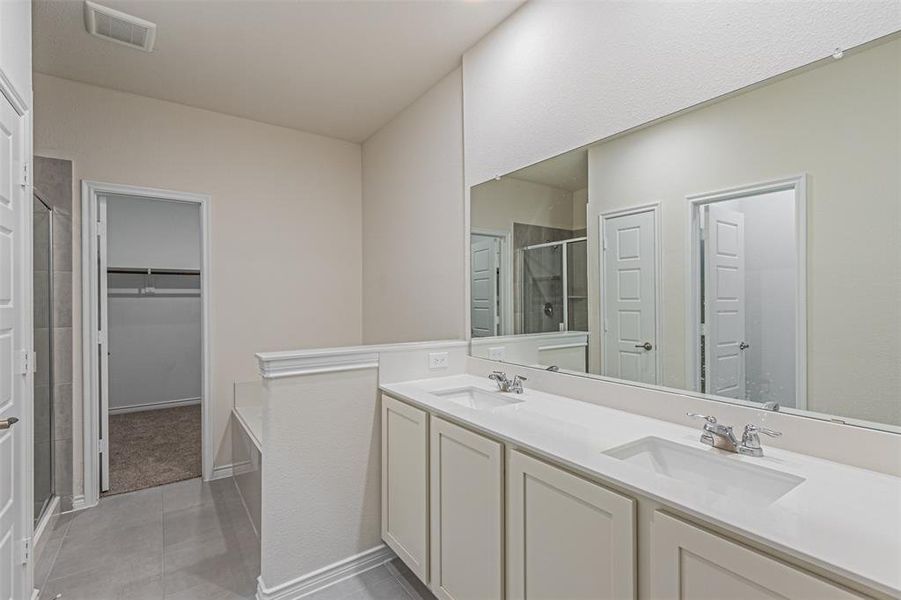 Bathroom with tile patterned floors, a shower with door, and dual bowl vanity