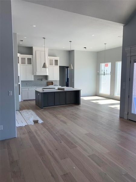 Kitchen with light wood-type flooring, a kitchen island with sink, white cabinetry, and decorative backsplash