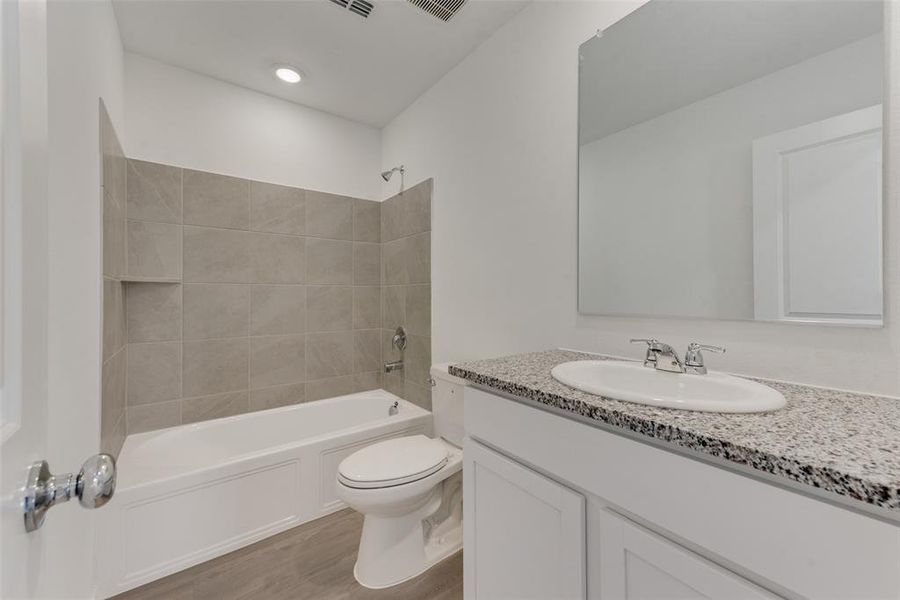 Full bathroom with hardwood / wood-style floors, vanity, tiled shower / bath combo, and toilet