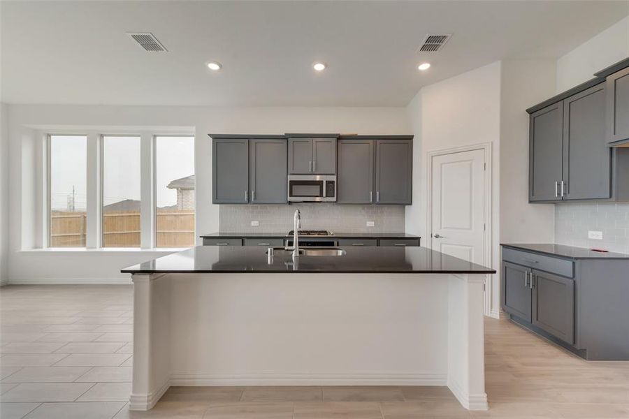 Kitchen with tasteful backsplash, a center island with sink, sink, and gray cabinetry