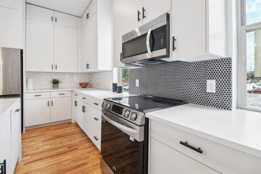 Kitchen with appliances with stainless steel finishes, light wood-type flooring, white cabinets, and backsplash