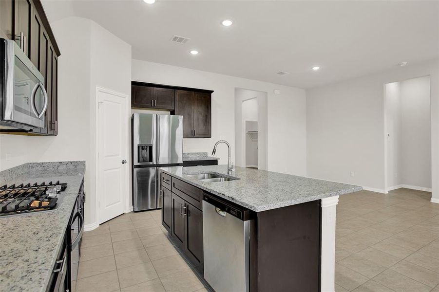 Kitchen with a center island with sink, light stone countertops, appliances with stainless steel finishes, sink, and light tile floors