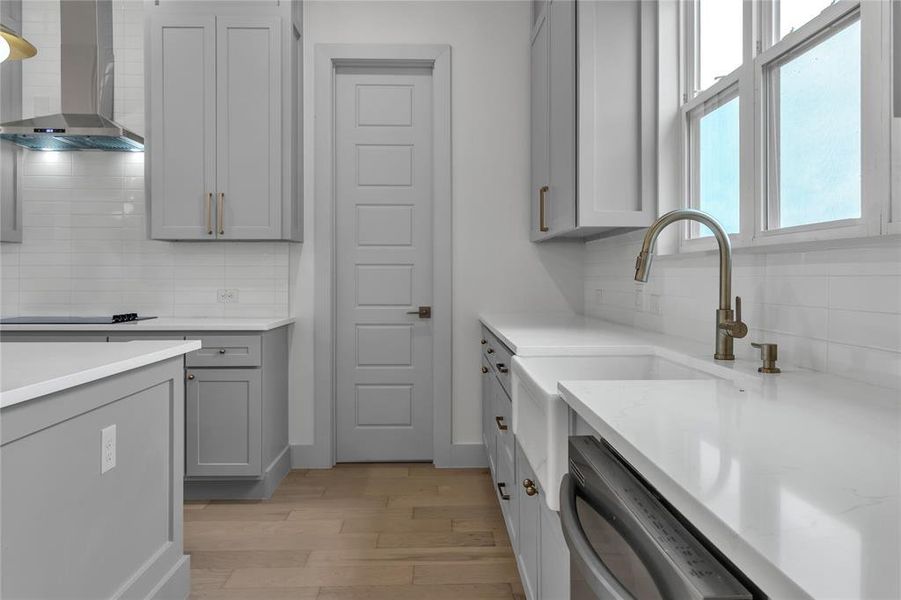 Kitchen with wall chimney range hood, gray cabinets, backsplash, light wood-type flooring, and dishwasher