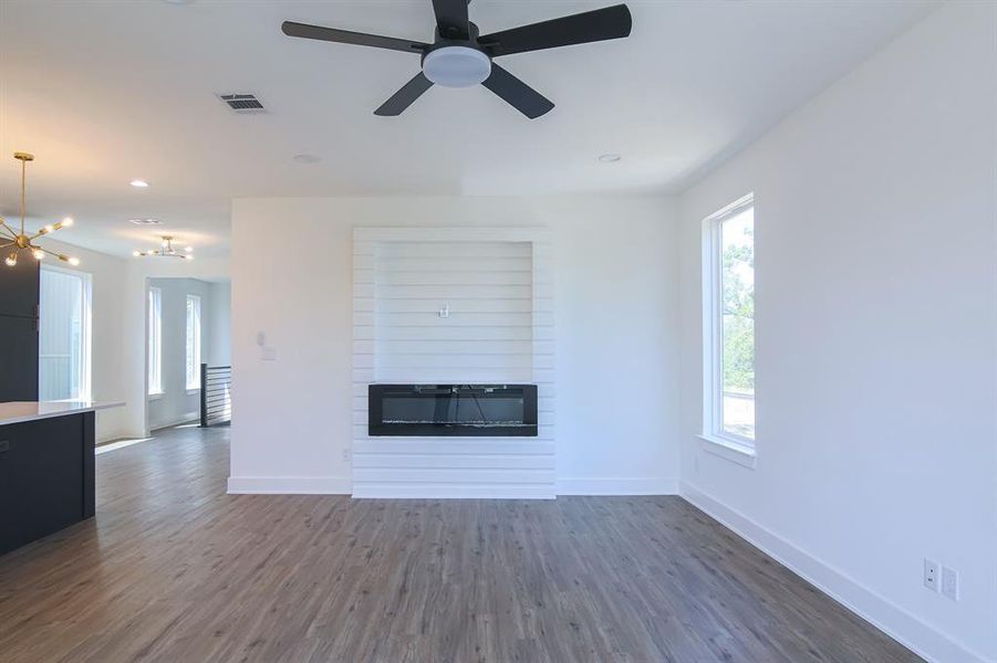 Unfurnished living room with ceiling fan with notable chandelier, dark hardwood / wood-style flooring, and a large fireplace