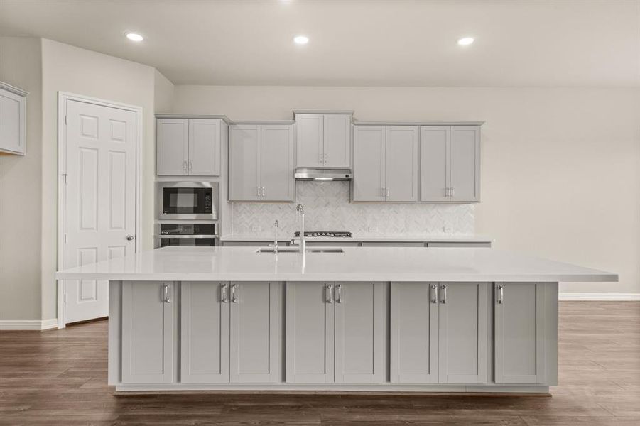 This light and bright kitchen features a large quartz island, light stained cabinets, a large sink overlooking your family room, recessed lighting, and beautiful backsplash.