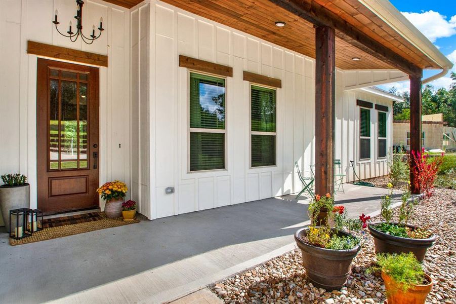 A welcoming front porch with a wooden door and multiple windows, complemented by a covered entryway with a classic chandelier and robust columns. The space is enhanced by decorative plants, offering a charming curb appeal.