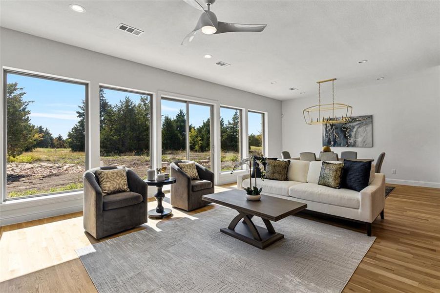 Living room with light hardwood / wood-style floors, a healthy amount of sunlight, and ceiling fan with notable chandelier