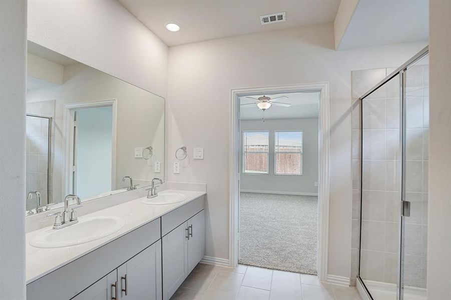 Primary bath has tile flooring, walk-in shower and double vanity