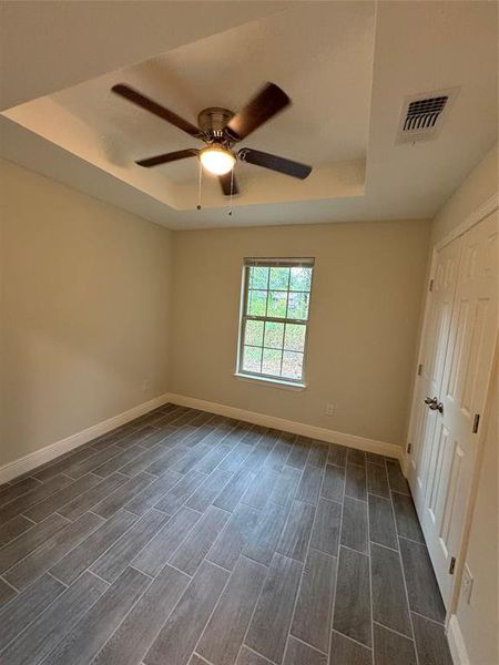 Unfurnished bedroom with ceiling fan, a raised ceiling, and dark wood-type flooring