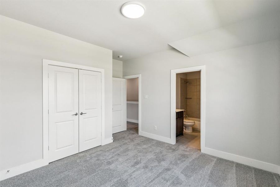 Unfurnished bedroom with a closet, light carpet, and ensuite bath