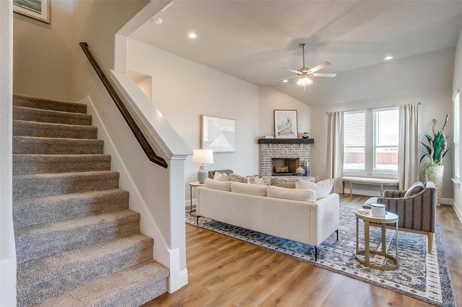 Living room with wood-type flooring, a brick fireplace, vaulted ceiling, and ceiling fan