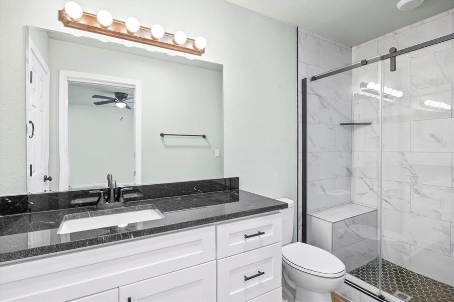 Bathroom with ceiling fan, toilet, vanity, and a shower with shower door