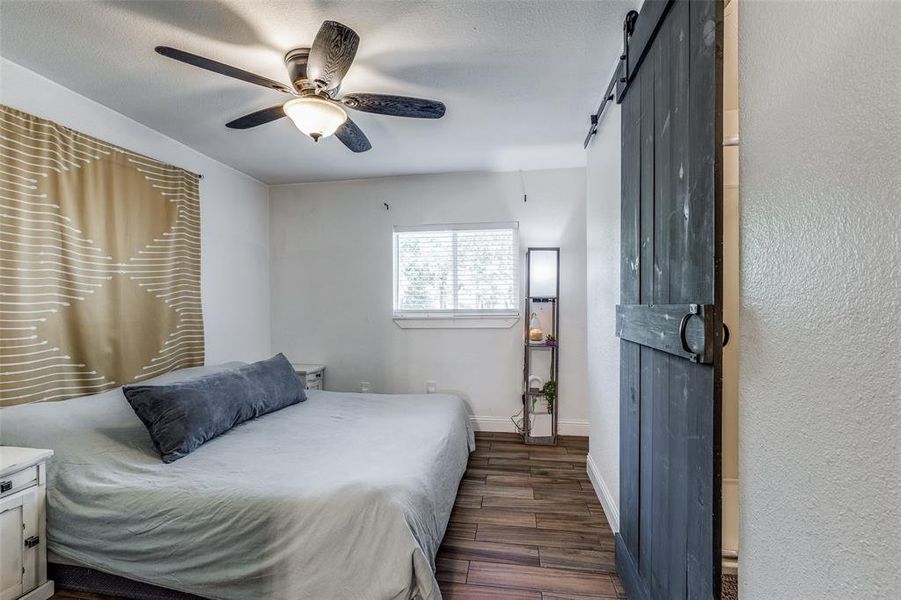 Bedroom with a barn door, ceiling fan, and dark hardwood / wood-style floors