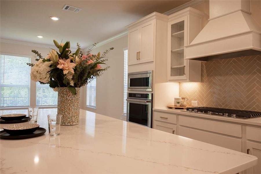 Kitchen with tasteful backsplash, appliances with stainless steel finishes, premium range hood, and white cabinets