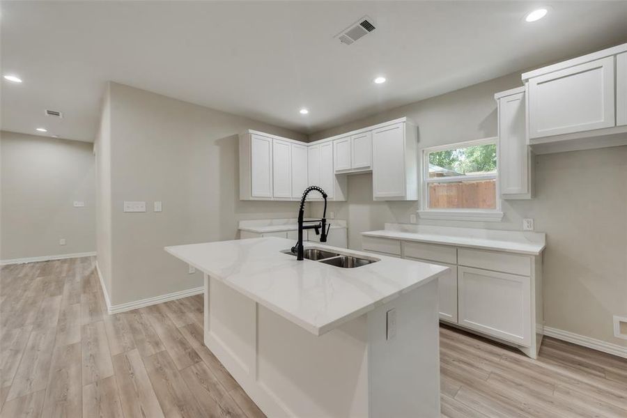 Kitchen featuring white cabinets, sink, light wood-type flooring, and an island with sink