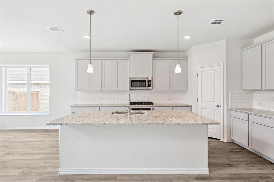 Kitchen with backsplash, a center island with sink, light wood-type flooring, and decorative light fixtures