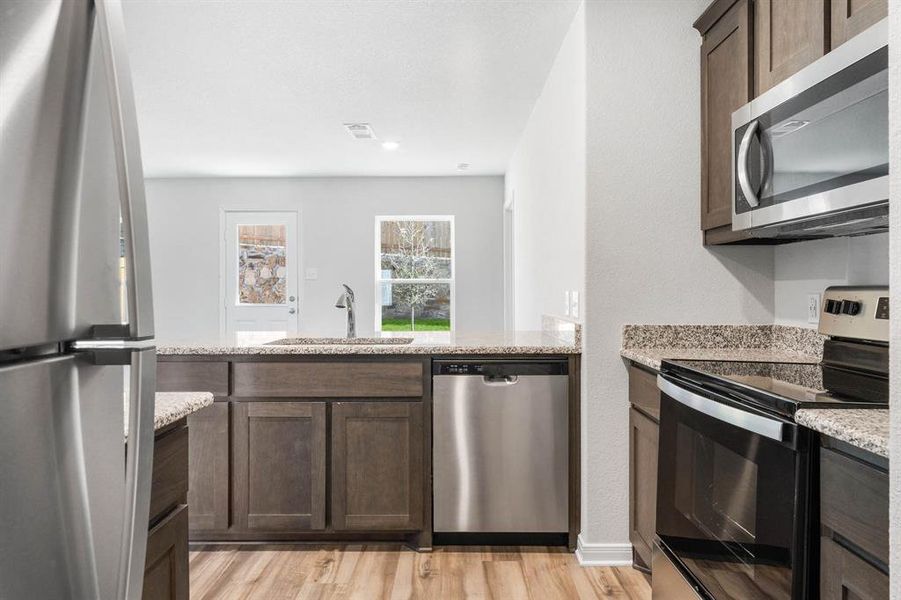 Kitchen featuring light hardwood / wood-style flooring, appliances with stainless steel finishes, light stone counters, sink, and dark brown cabinets