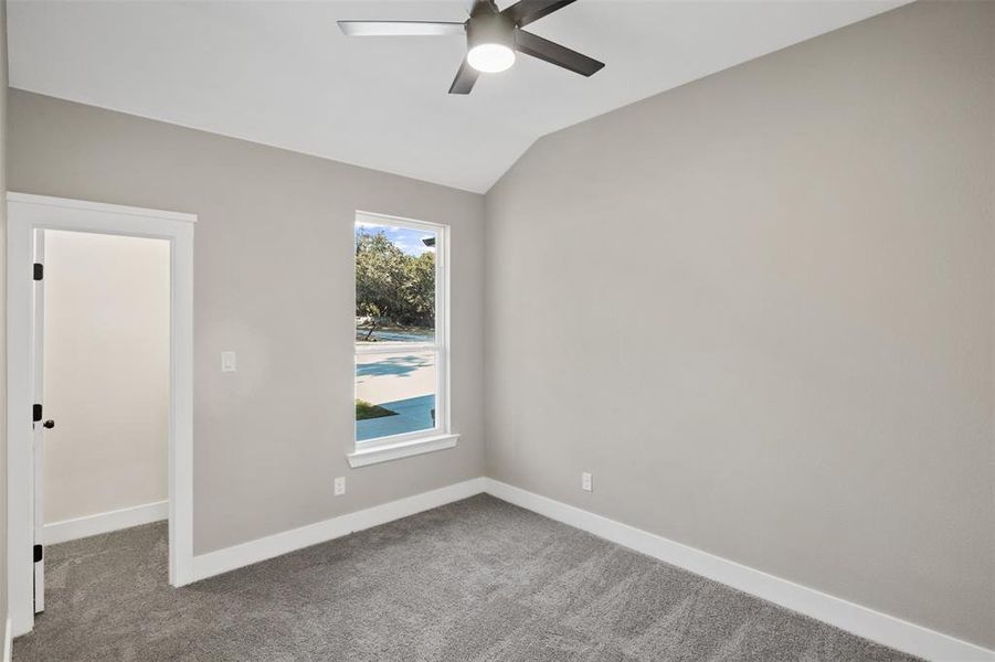 Carpeted spare room featuring ceiling fan and vaulted ceiling