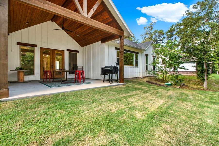 This home features a spacious covered patio with exposed wooden beams, perfect for outdoor dining and relaxation, and a well-maintained lawn that offers ample space for activities. The exterior presents a modern farmhouse style with clean lines and large windows.