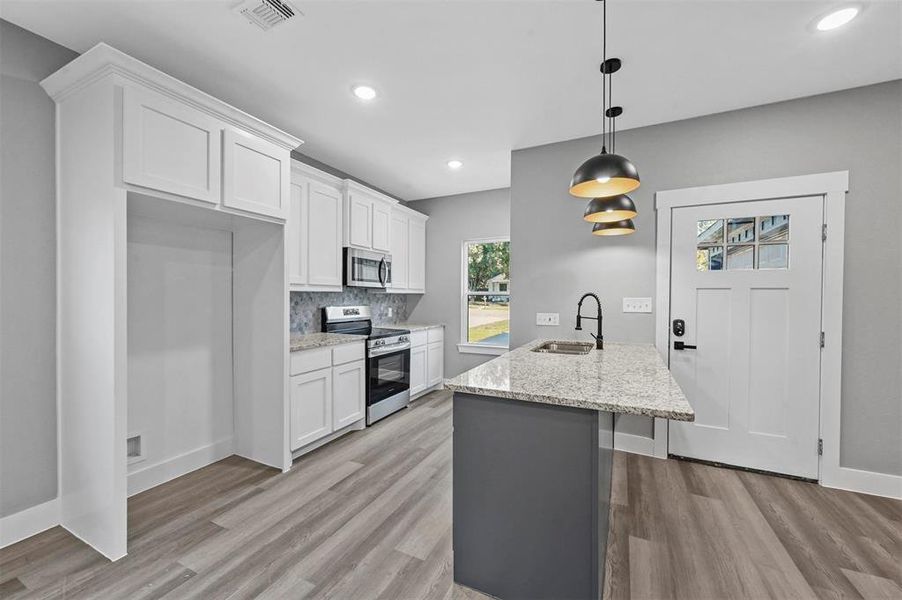 Kitchen featuring white cabinetry, light stone counters, stainless steel appliances, light wood-type flooring, and decorative light fixtures