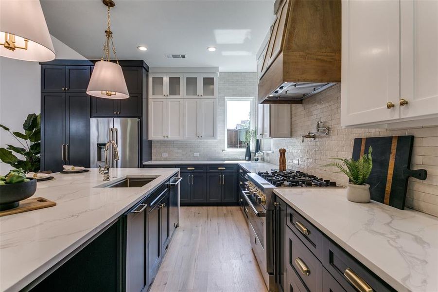 Kitchen with custom range hood, light hardwood / wood-style flooring, tasteful backsplash, high end appliances, and sink