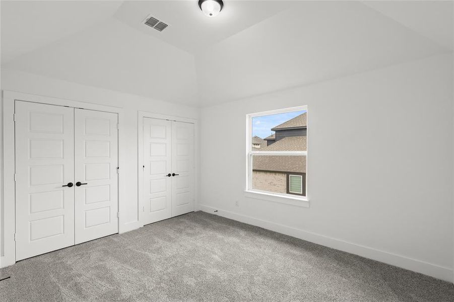 Unfurnished bedroom featuring lofted ceiling, carpet floors, and two closets