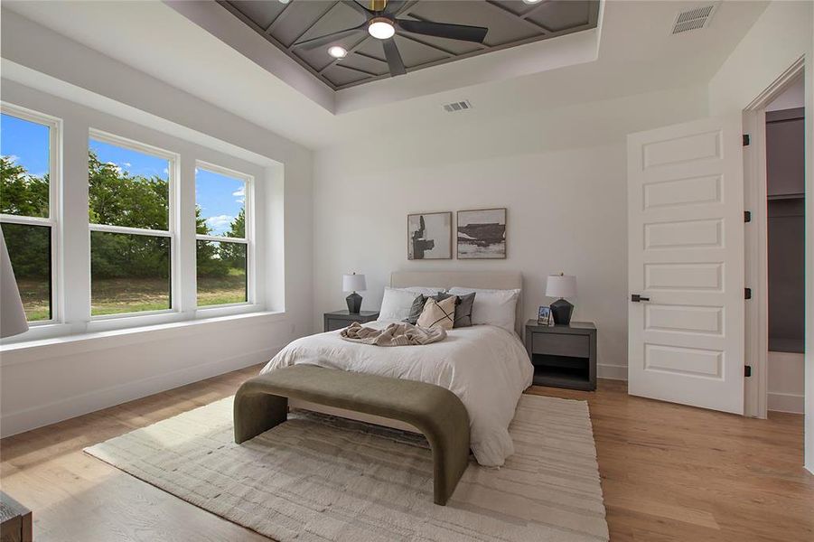 Bedroom featuring ceiling fan, a tray ceiling, and light hardwood / wood-style flooring
