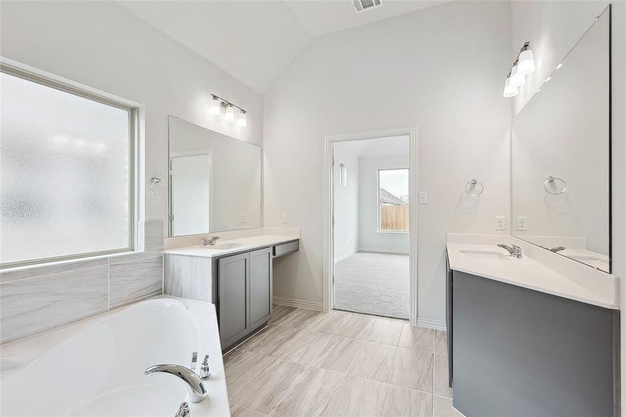 Bathroom with tile flooring, vaulted ceiling, a washtub, oversized vanity, and dual sinks