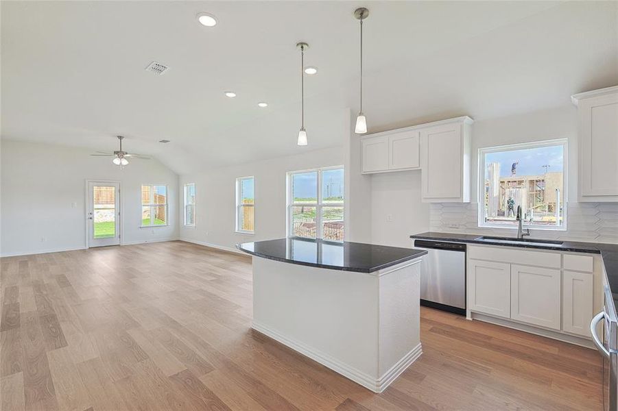 Kitchen featuring backsplash, stainless steel dishwasher, a center island, light wood-type flooring, and white cabinets