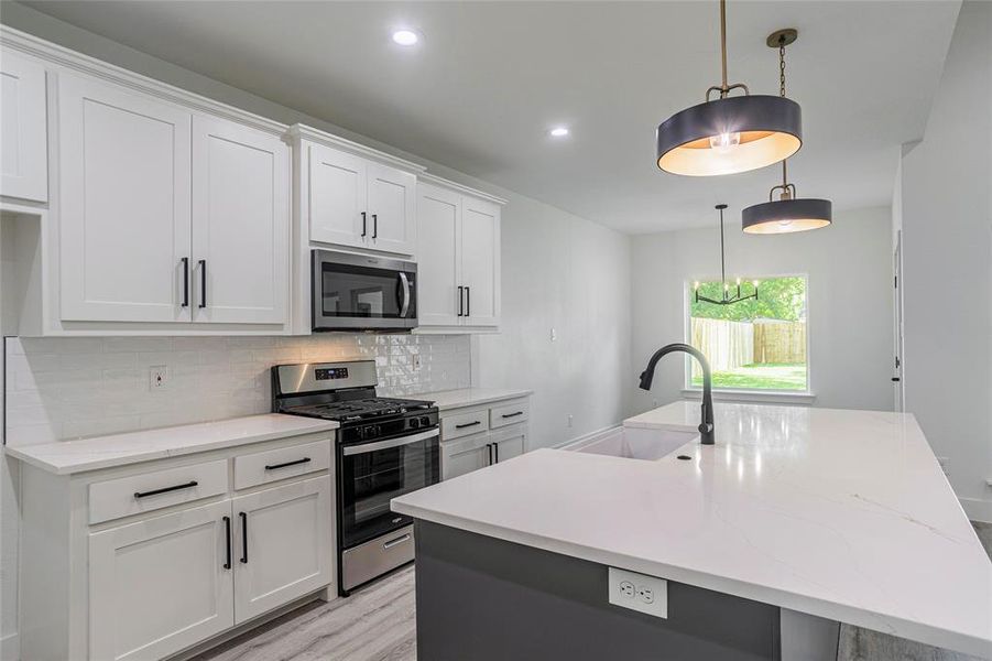 Kitchen with appliances with stainless steel finishes, light hardwood / wood-style flooring, sink, backsplash, and a kitchen island with sink