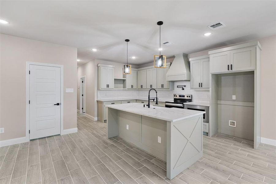Kitchen featuring white cabinetry, a center island with sink, premium range hood, electric stove, and tasteful backsplash