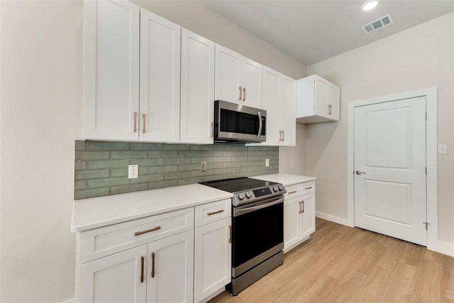 Kitchen featuring appliances with stainless steel finishes, backsplash, light hardwood / wood-style floors, and white cabinetry