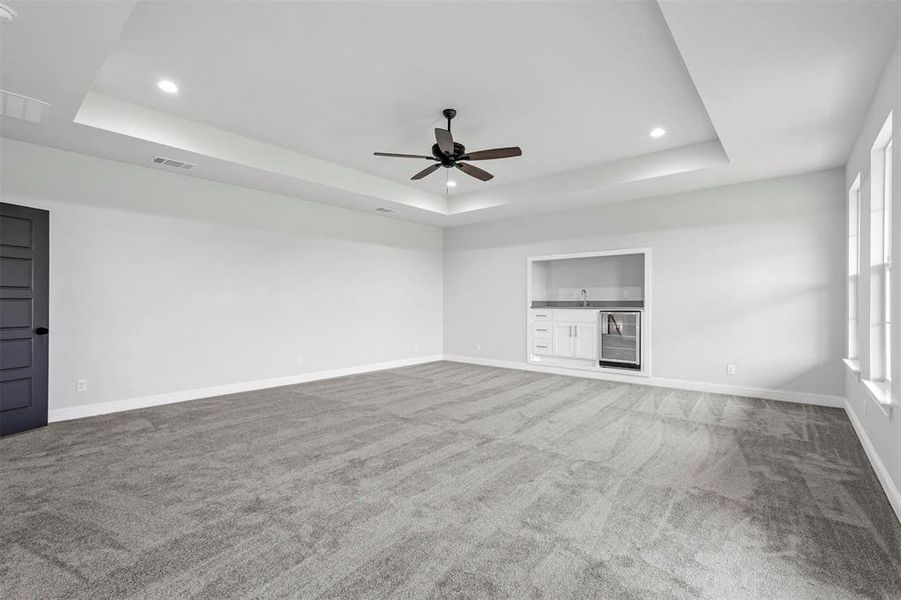 Unfurnished living room featuring carpet flooring, ceiling fan, a raised ceiling, wine cooler, and sink