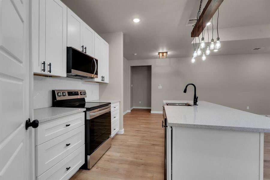 Kitchen featuring light wood-type flooring, decorative light fixtures, stainless steel appliances, sink, and white cabinets