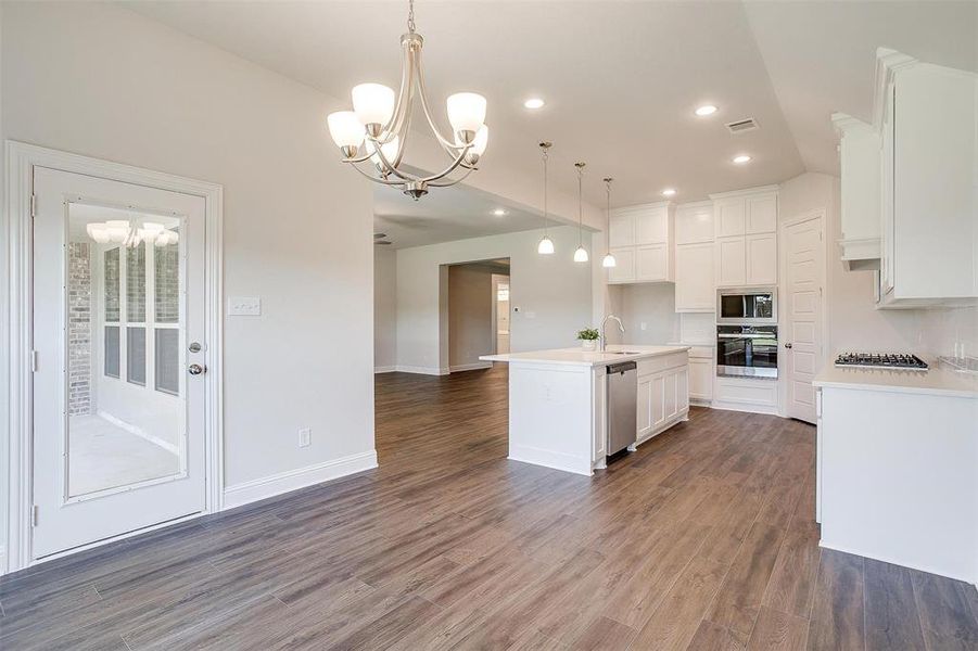 Kitchen with an island with sink, stainless steel appliances, white cabinetry, and dark wood-type flooring