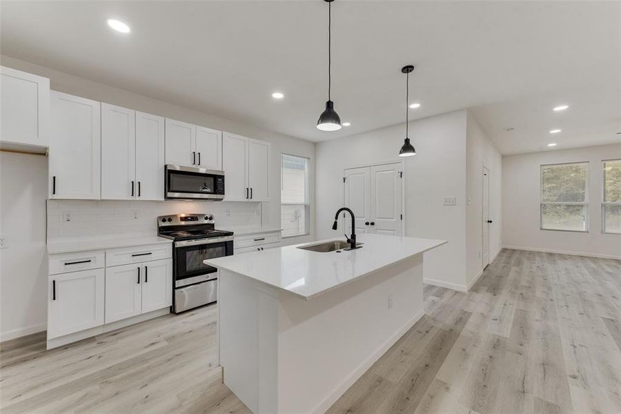 Kitchen with decorative light fixtures, stainless steel appliances, sink, and a wealth of natural light