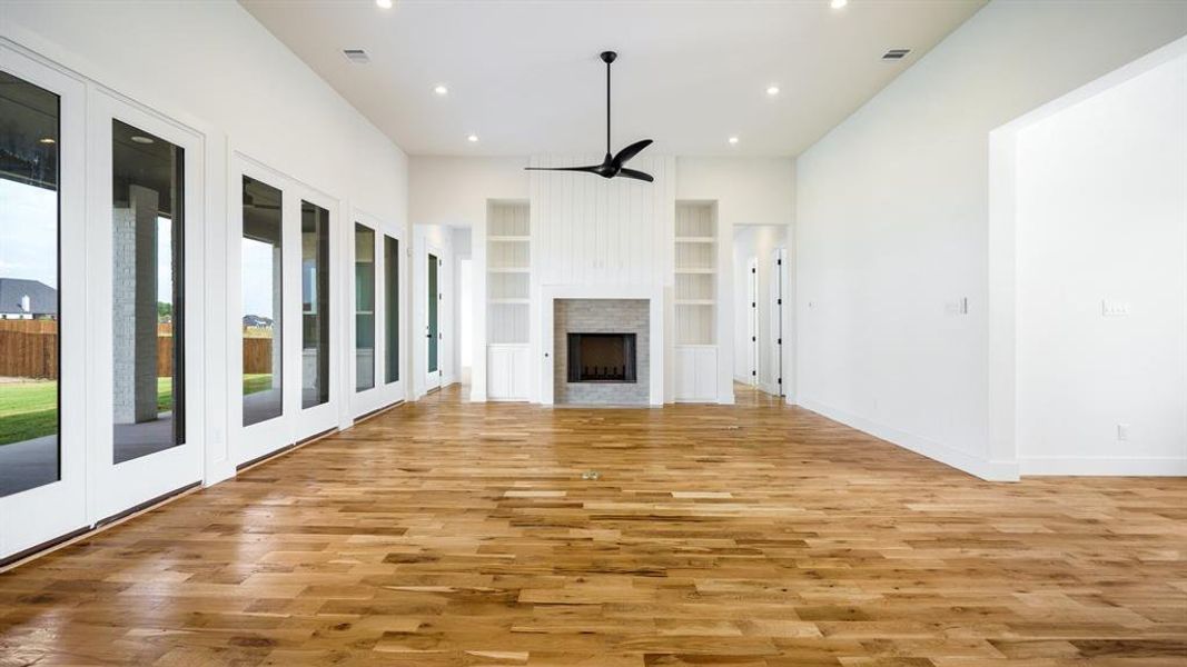 Unfurnished living room featuring light wood-type flooring, ceiling fan, and built in shelves