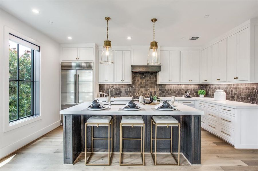 Kitchen with an island with sink, backsplash, built in refrigerator, and white cabinetry