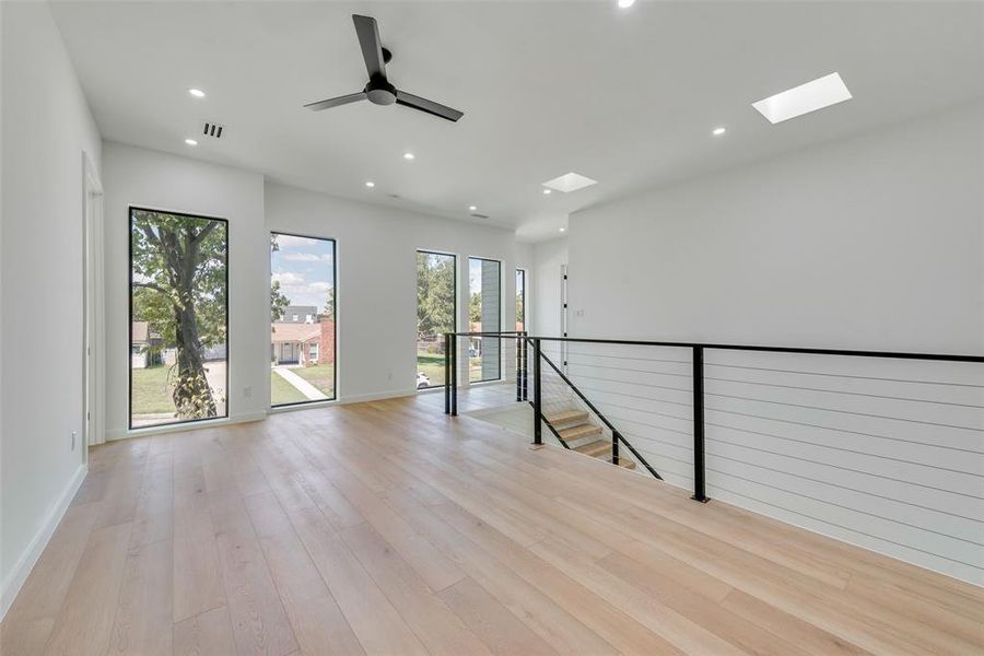 Spare room with light hardwood / wood-style floors, ceiling fan, and a skylight