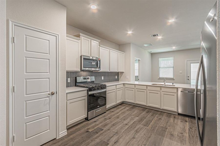 Kitchen with appliances with stainless steel finishes, white cabinets, sink, decorative backsplash, and wood-type flooring