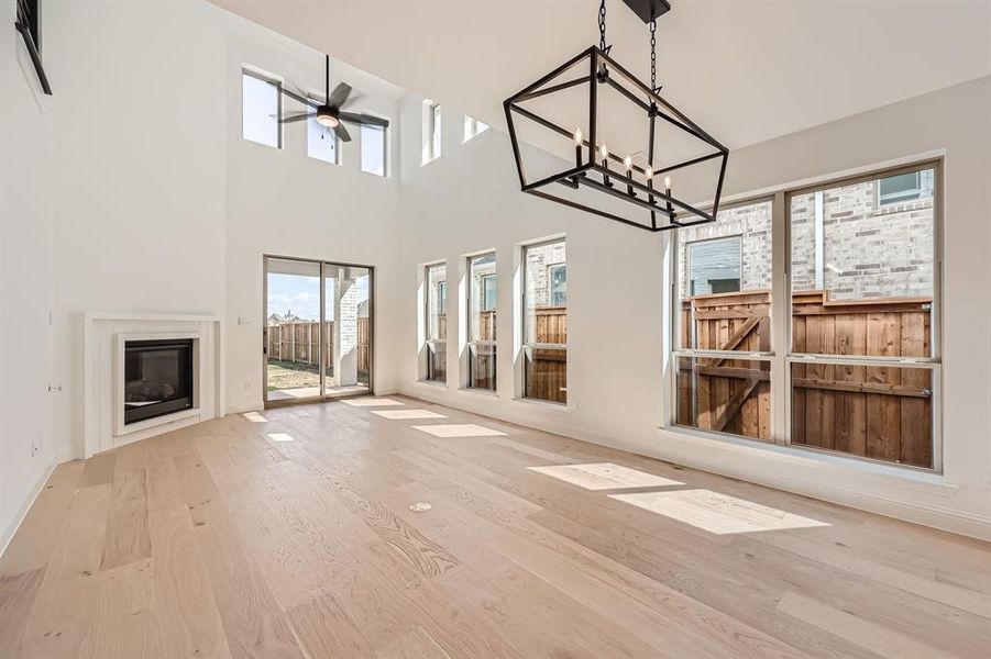 Unfurnished living room featuring ceiling fan with notable chandelier, a high ceiling, and light hardwood / wood-style floors