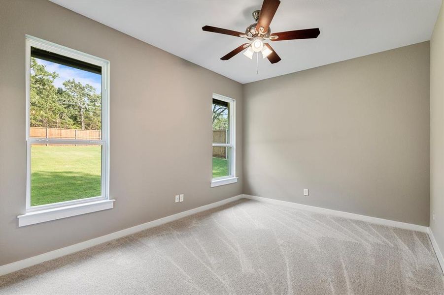 Carpeted spare room featuring plenty of natural light and ceiling fan