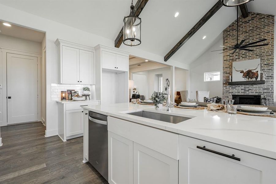 Kitchen featuring vaulted ceiling with beams, white cabinetry, light stone countertops, and sink