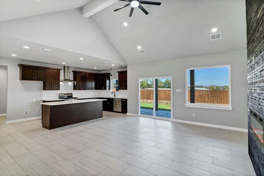 Kitchen featuring beam ceiling, wall chimney exhaust hood, high vaulted ceiling, appliances with stainless steel finishes, and a center island