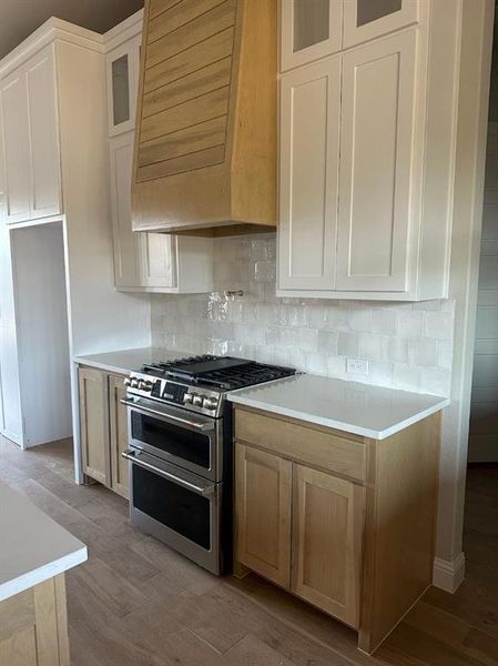 Kitchen featuring premium range hood, light wood-type flooring, white cabinetry, and double oven range