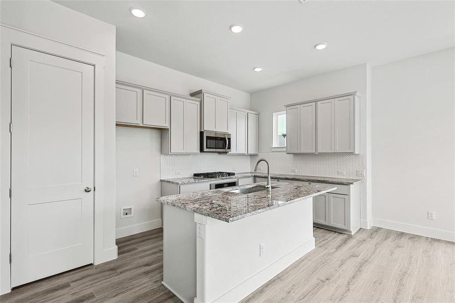 Kitchen featuring sink, a kitchen island with sink, light stone countertops, and light hardwood / wood-style floors