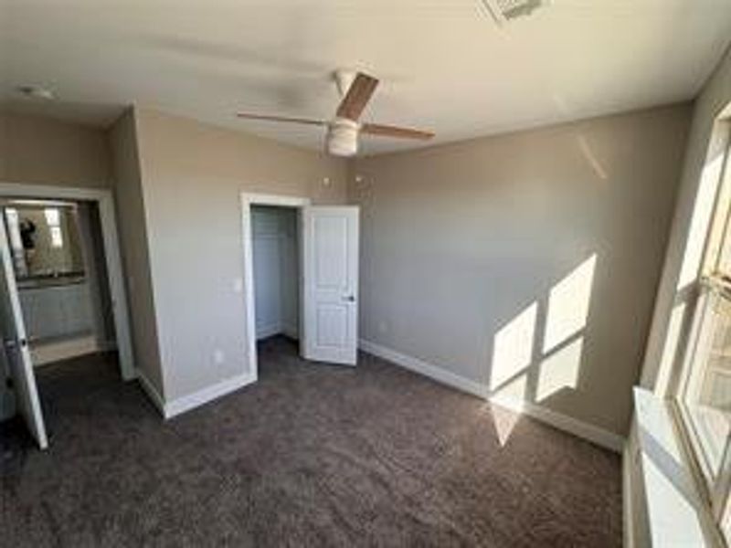 Unfurnished bedroom featuring dark carpet, a closet, ceiling fan, and a walk in closet