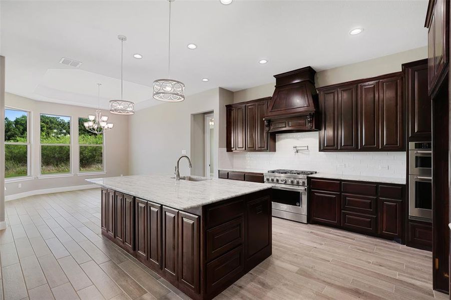 Kitchen with appliances with stainless steel finishes, decorative light fixtures, backsplash, an island with sink, and custom range hood