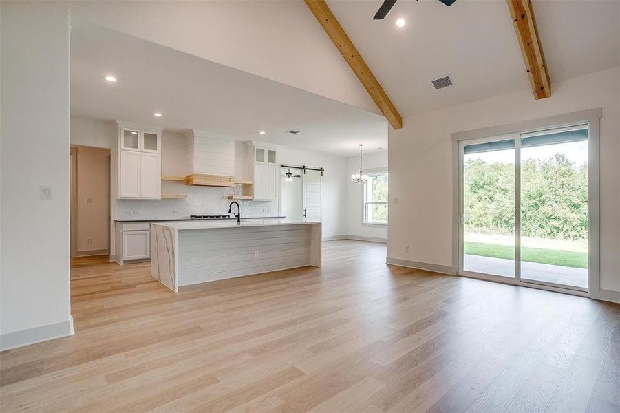 Kitchen featuring beam ceiling, a kitchen island with sink, white cabinetry, and light wood-type flooring