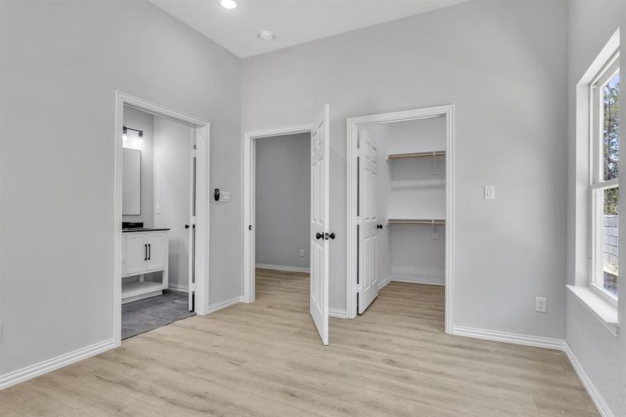 Unfurnished bedroom with a spacious closet, a closet, connected bathroom, and light hardwood / wood-style floors
